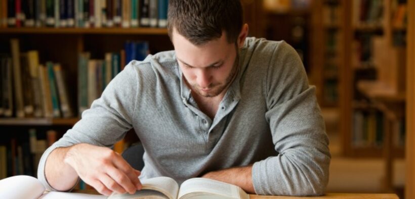 Male college student studying in library.