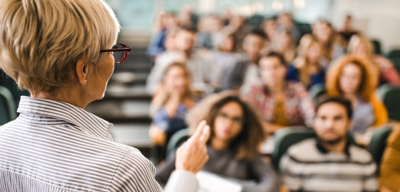 Over-the-shoulder view of a female professor lecturing to an auditorium